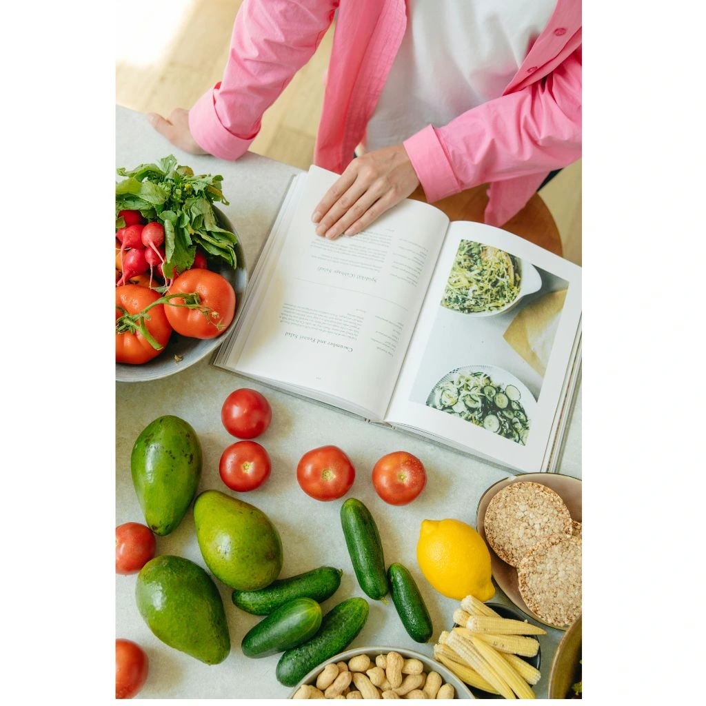 hand of a person on an open book near fresh vegetables for healthy recipes.